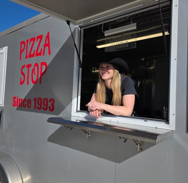 a girl wearing a cowboy hat smiling from the window of a grey pizza truck