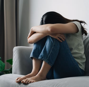 Frau sitzt auf einem Sofa, hat die Knie angezogen und den Kopf auf die Arme gelegt – Ausdruck von Er