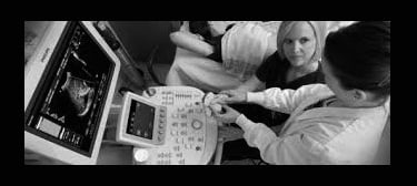 Instructor teaching ultrasound student at bedside.