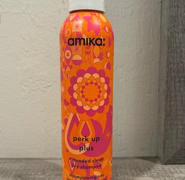 orange and pink Amika Perk Up Plus Dry Shampoo bottles on a bathroom counter