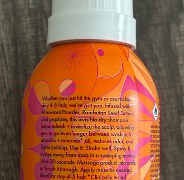 orange and pink Amika Perk Up Plus Dry Shampoo bottles on a bathroom counter