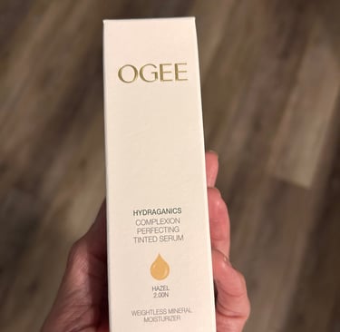 Hand holding Ogee Complexion Perfecting Tinted Serum box in shade Hazel 2.00N.