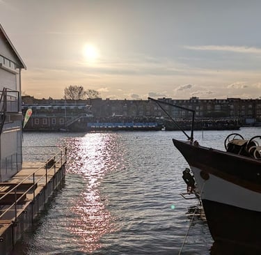 Maison flottante moderne et péniche traditionnelle sur un canal d'Amsterdam au coucher du soleil.