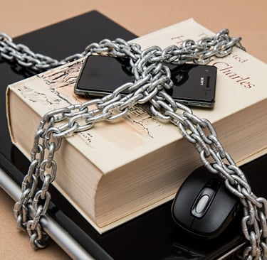 a closed laptop with a, book on top of it, and a cell phone all secured by a large chain and lock