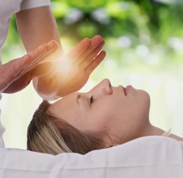 Hands of Reiki Practitioner beaming golden-white  light to a woman's forehead who is laying down