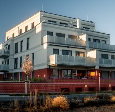 Mehrfamilienhaus mit roten Klinkersteinen im Erdgeschoss und weißen Fassaden mit Balkonen 