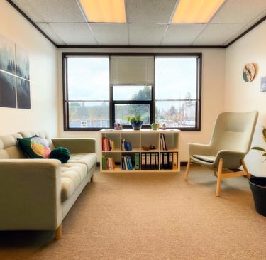 Inside view of the space with a couch, a bookcase and a chair in front of large windows