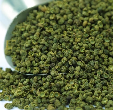 A metal scoop overflowing with dried green Sichuan peppercorns, showcasing their unique husks and texture.