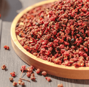 A heap of dried red Sichuan peppers on a round wooden tray, highlighting the spice texture.