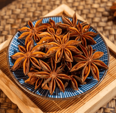 Dried whole star anise pods in a blue ceramic bowl on a wooden tray for cooking and spice display.