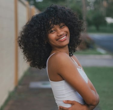 Smiling Black woman with curly hair standing outdoors, symbolizing joy and self-worth.