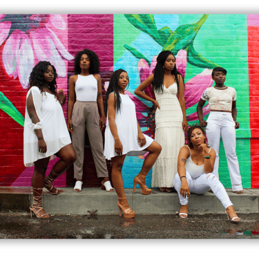 a group of women standing in front of a colorful mural