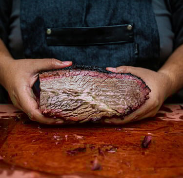pitmaster holding brisket, showing smoke ring and fat marbling