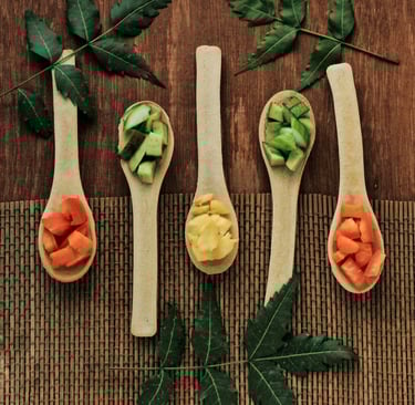 Flat lay of fresh chopped vegetables on wooden spoons with green neem leaves on a rustic mat.