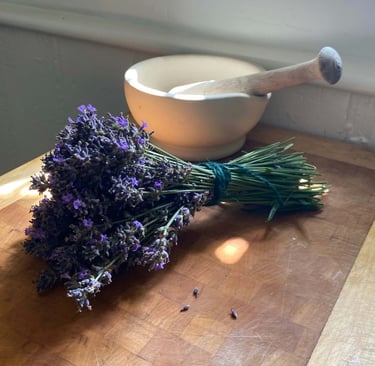 A fresh bundle of dried lavender flowers tied with twine next to a mortar and pestle on a wooden cutting board.