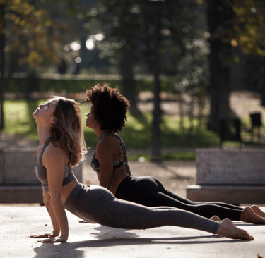 two women doing upward-facing dog yoga pose in a park