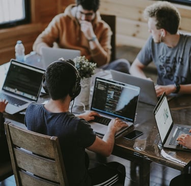 A group of people sitting around a table with laptops, discussing brand confusion and strategy.