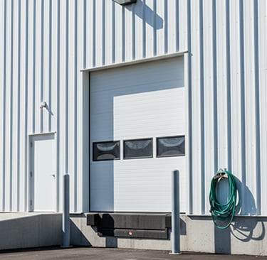 White industrial warehouse loading dock with a sectional overhead door and metal siding.
