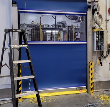 Blue industrial high-speed roll-up door with a clear vision panel installed in a warehouse facility.