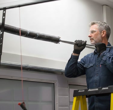 Professional technician on a ladder installing a heavy-duty garage door torsion spring.