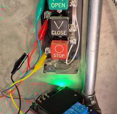 Industrial control station with open, close, and stop buttons wired to an electrical relay using alligator clips.