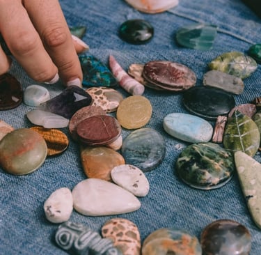 Una mano seleccionando piedras preciosas pulidas y cristales curativos exhibidos sobre una tela azul