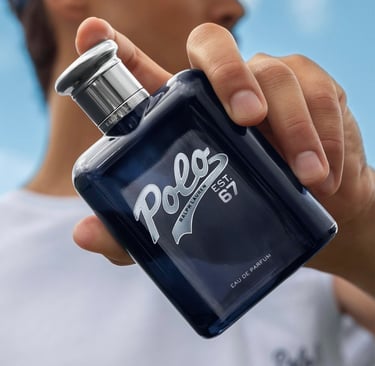 A hand holding a bottle of Ralph Lauren Polo Est. 67 Eau de Parfum men's fragrance against a blue sky.