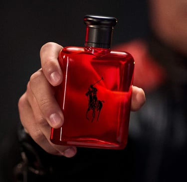 A man's hand holding a red Ralph Lauren Polo Red perfume bottle with the iconic polo player logo.