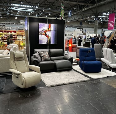 Modern living room furniture display at a trade fair featuring recliners, sofas, and area rugs.