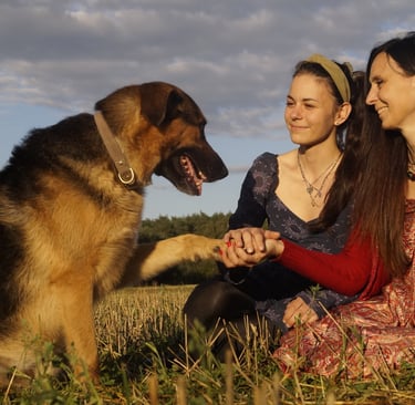 2 kobiety siedzące na polanie i pies podający im łapę 