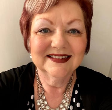 Photo of Debbie in front of a blank wall, wearing business black and jewelry.