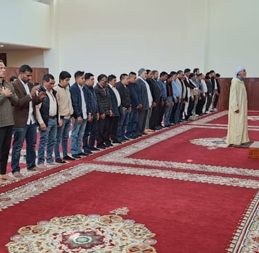 a group of men standing in line performing salat at Imam Malik Mosque