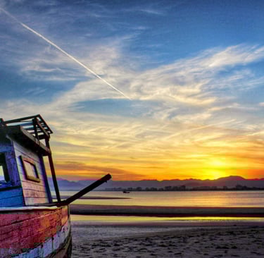 Barco encalhado na areia com entardecer ao fundo