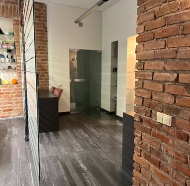 Modern office interior featuring exposed red brick walls, glass partitions, and dark wood flooring.