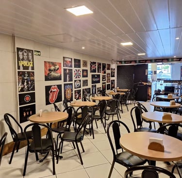 Área da cafeteria com mesas cadeiras e pôsteres de rock no Studio Brothers em Porto Alegre