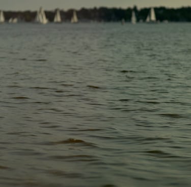 Film still from "Desire for Belonging" by Tina Bikic of a woman dancing through water with sailboats in the distance.