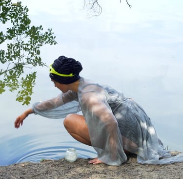 ilm still from "Fear" by Tina Bikic of a performer in a sheer garment crouching by the lake, reaching to the water.