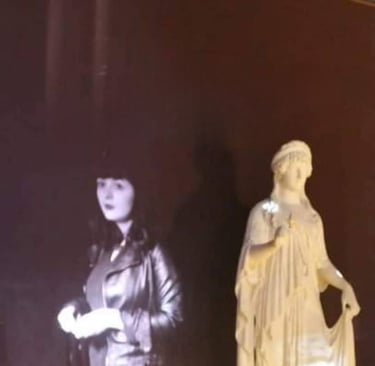 Projection of Tina Bikic beside a classical statue in a museum installation.