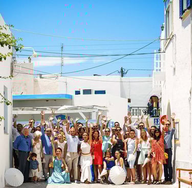 Foto di gruppo di tutti gli invitati del matrimonio che salutano verso il fotografo, nel bianco dell'isola greca Antiparos