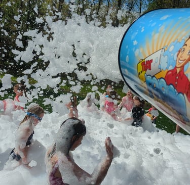 a group of children playing in foam with a foam machine blasting at a birthday party