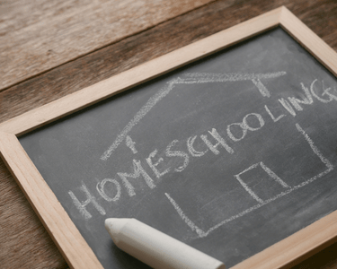 Homeschooling word and house outline drawn in chalk on a black chalkboard on a wooden table.
