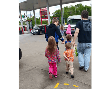 A family with several small children walking through a gas station parking lot together.
