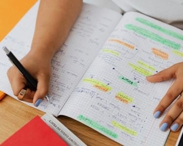 Student writing in a notebook with color-coded highlights for exam study and organization.