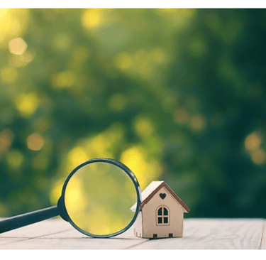 Petite maison sur une table en bois avec une loupe à côté, sur un fond flou d'arbres ou feuilles
