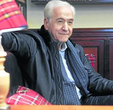 a man in a black jacket and tie dye on a chair