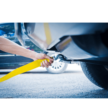 Image of a tow truck operator hooking a winch to the under carriage of a stranded vehicle.
