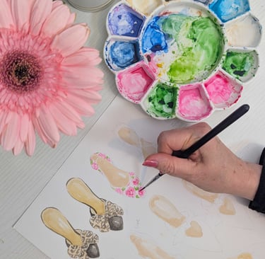 Hand painting watercolor shoes with palette and pink flower in background.