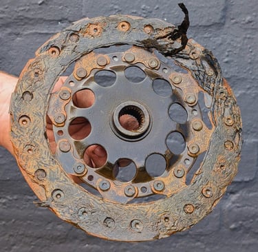A heavily worn and damaged car clutch friction disc with frayed lining and rust.