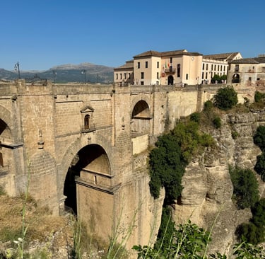 The historic Puente Nuevo stone bridge spans the El Tajo gorge in Ronda, Spain, under a clear blue sky.
