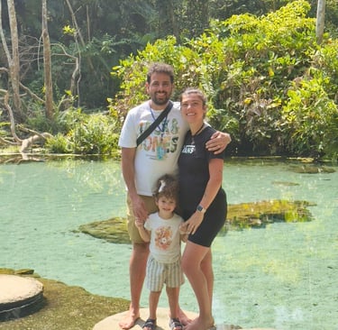 A happy family of three poses on stepping stones in a clear tropical lagoon surrounded by lush jungle.